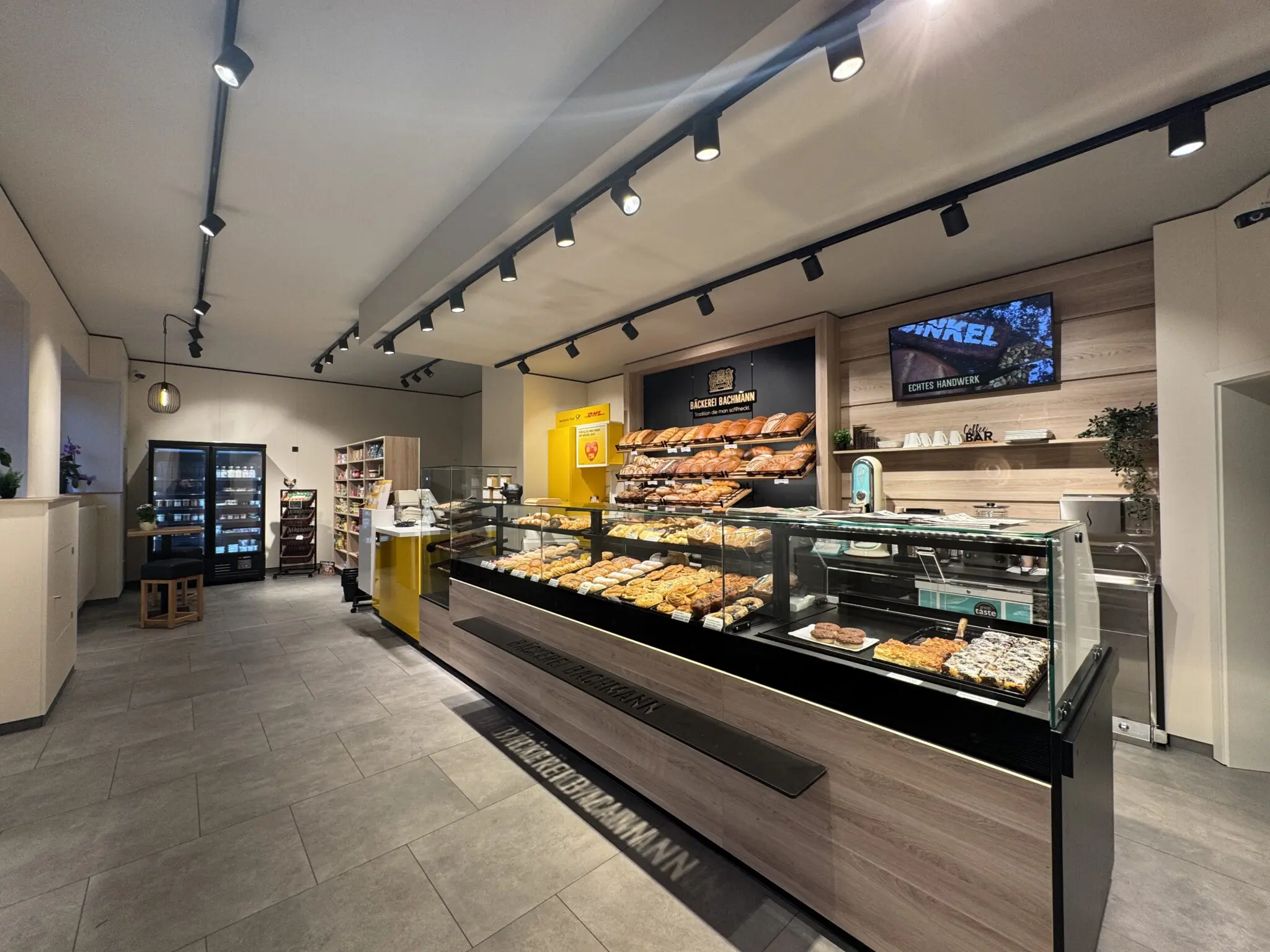 Thekenbereich der Bäckerei Bachmann in Küllstedt mit Backwaren, Brotregal und digitalen Menüanzeigen