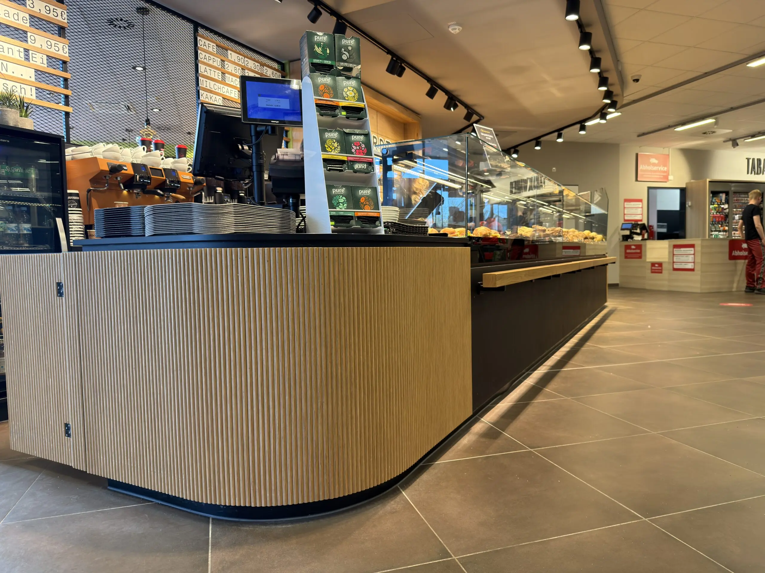 Gerundete Thekenfront der Bäckerei Eckhardt mit Holzlamellen, Kaffeezone und Verkaufstheke im Hintergrund.