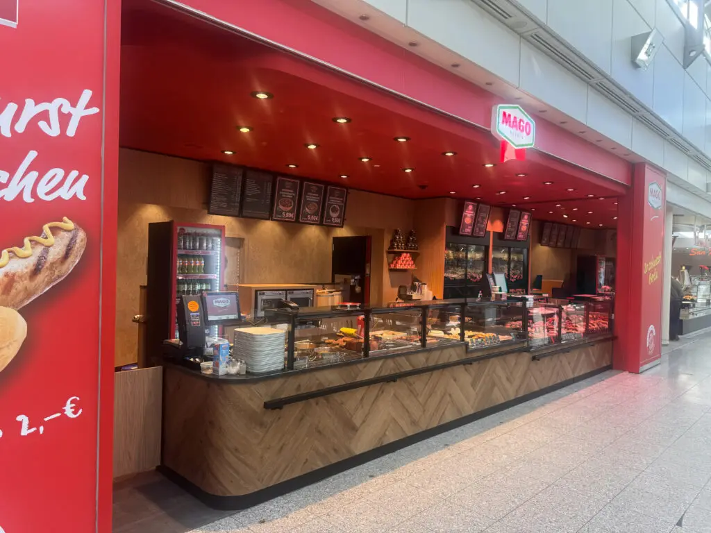 Blick auf die Fleischerei MAGO in Berlin mit roter Gestaltung, langer Theke und Produkten in der Auslage.