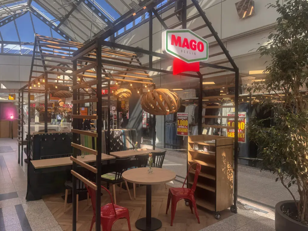 Sitzbereich der Fleischerei MAGO in Berlin mit Holzkonstruktion, Tischen, roten Stühlen und beleuchtetem Logo.