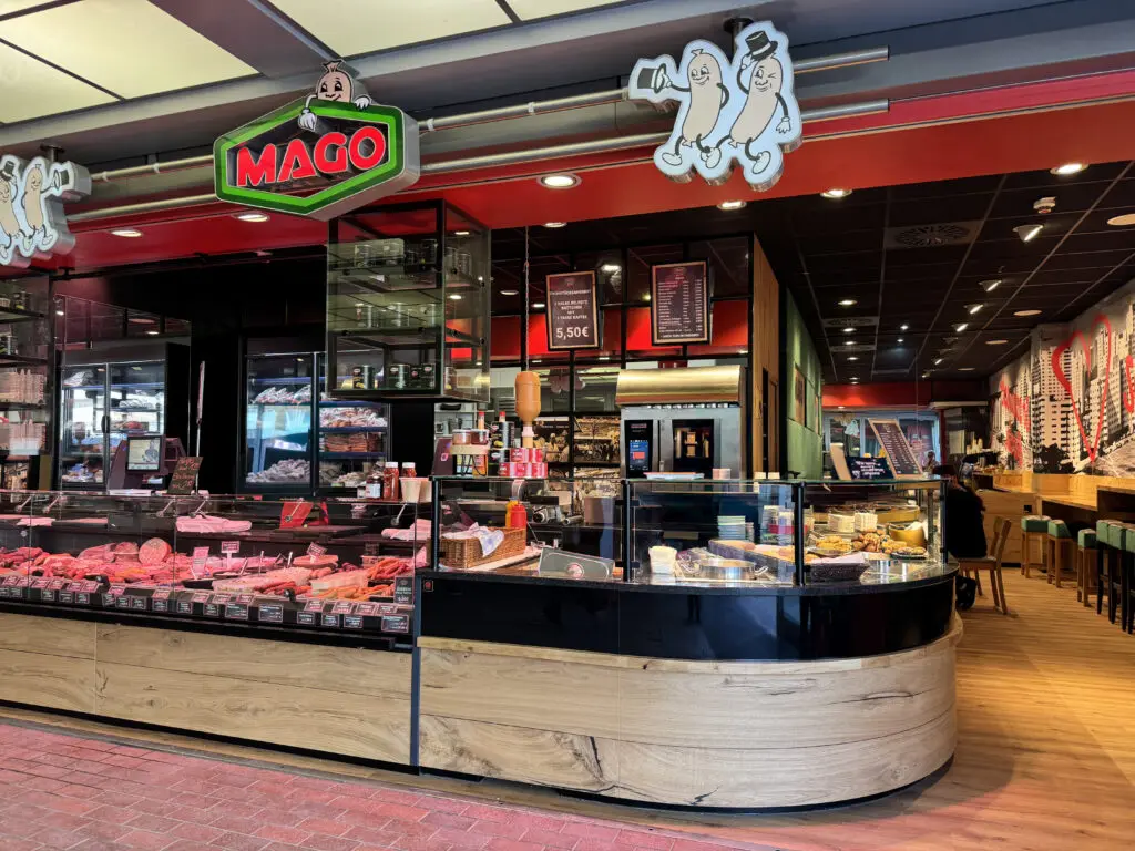 Fleischereieinrichtung von MAGO im Märkischen Zentrum Berlin mit gerundeter Theke, Holzfront, Frischeauslage und Sitzbereich im Hintergrund.