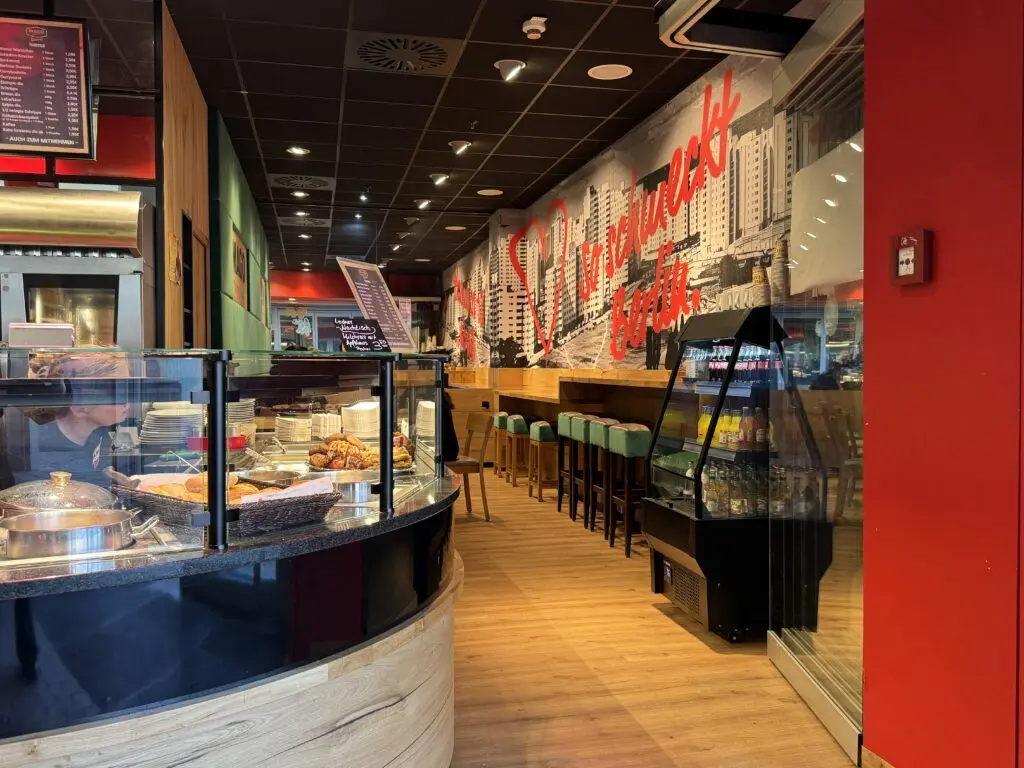 Sitzbereich der Fleischerei MAGO im Märkischen Zentrum Berlin mit langer Holztheke, Hockern und Wandgrafik im Berliner Stil.