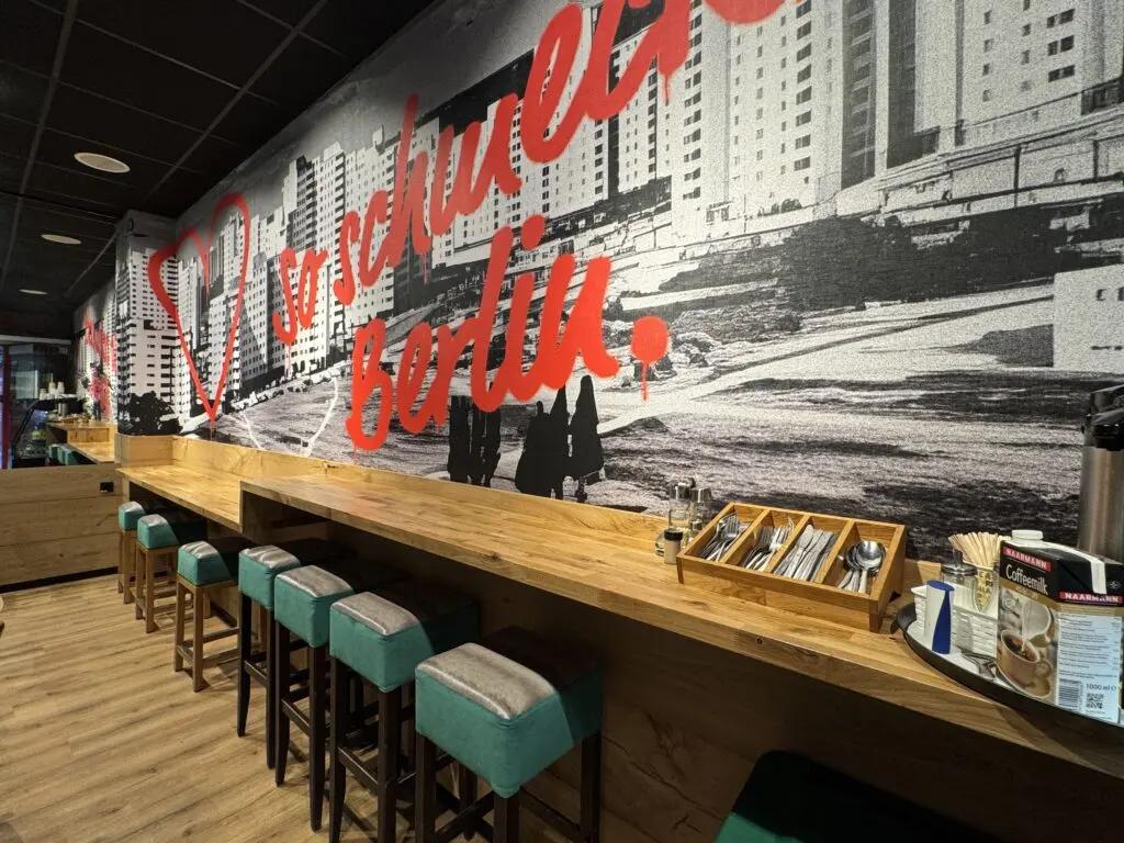 Sitzbereich von MAGO im Märkischen Zentrum Berlin mit langer Holztheke, Hockern und Wandgrafik im Berliner Stil.