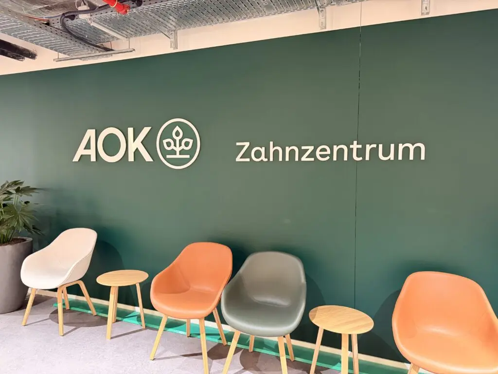 Wartebereich im Zahnzentrum der AOK Düsseldorf Stadtmitte mit grüner Wand, Sitzplätzen und moderner Einrichtung.