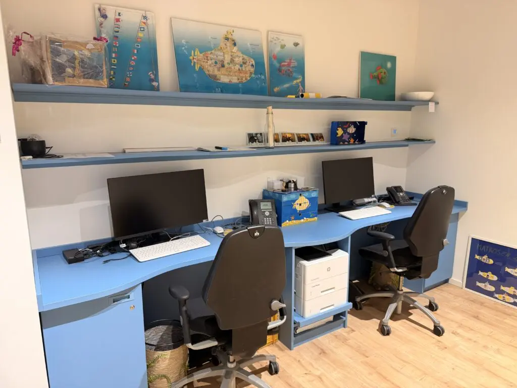 Arbeitsbereich im AOK U-Boot Gesundheitszentrum für Kinder mit hellblauen Schreibtischen, Regalen und maritimen Gestaltungselementen.