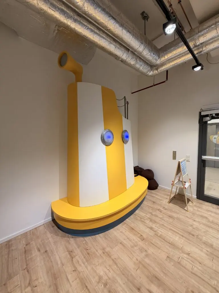 U-Boot-Sitzbank im AOK U-Boot Gesundheitszentrum für Kinder mit gelber Gestaltung, Bullaugen und maritimer Einrichtung.