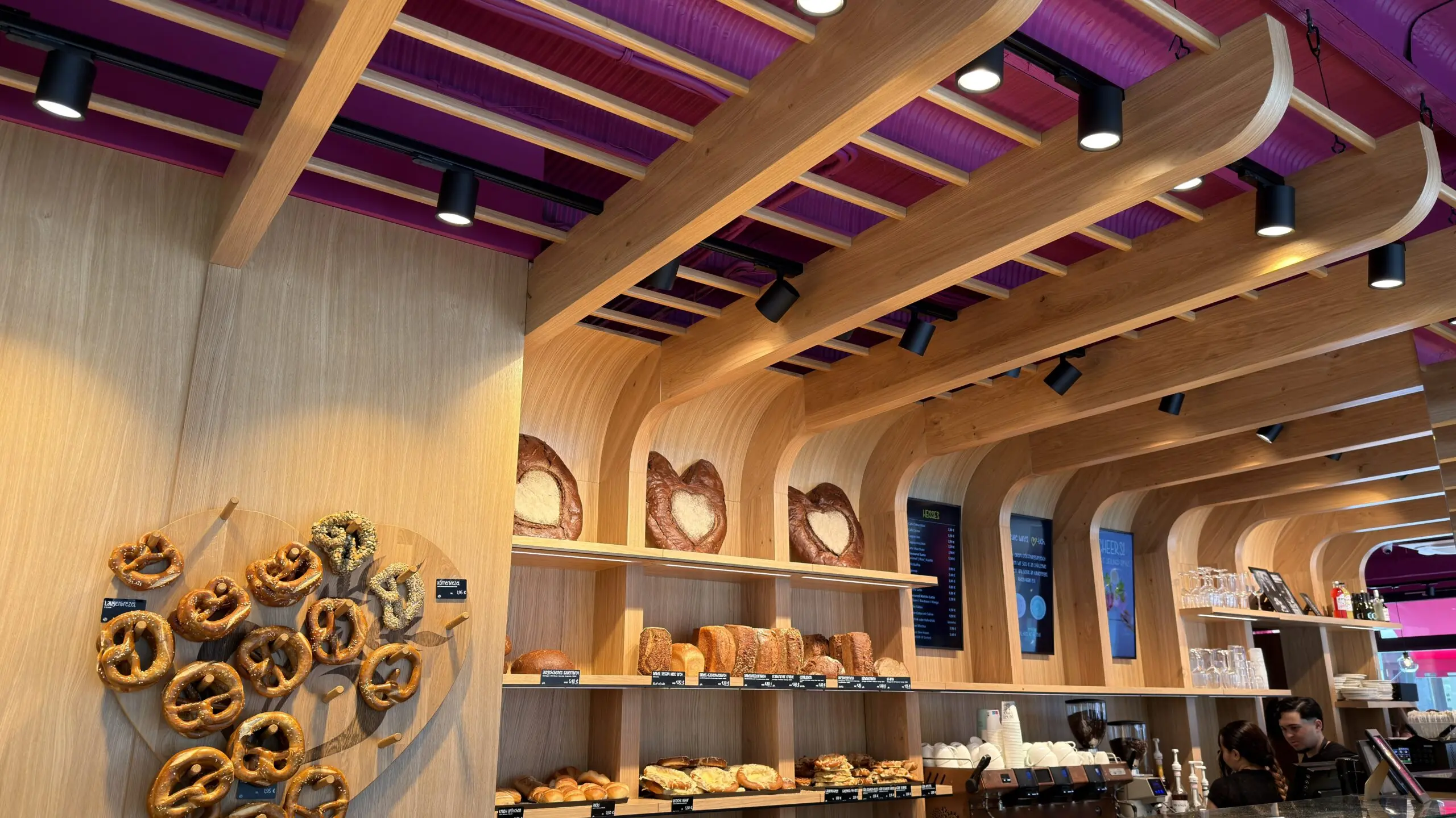 Bäckerei Huck in Frankfurt mit abgehangener Design-Decke aus Holz, integrierten Spots und Brezel-Präsentation an der Rückwand.