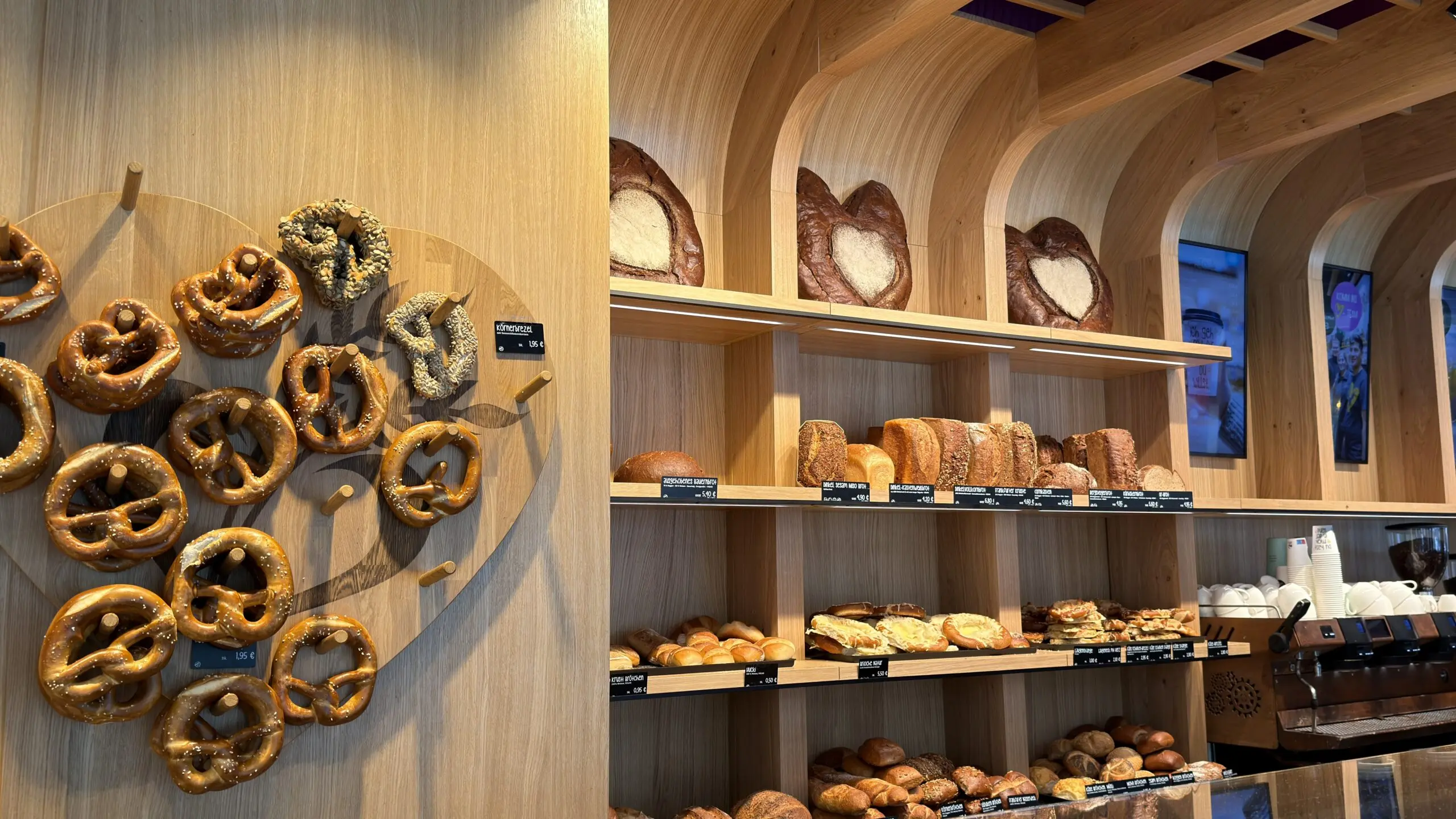 Brotregal der Bäckerei Huck in Frankfurt mit heller Holzrückwand, Brezel-Präsentation und Backwaren in offenen Regalen.