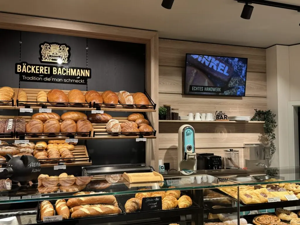 Bäckereieinrichtung der Bäckerei Bachmann in Küllstedt mit gefülltem Brotregal, Holzoptik und schwarzer Akzentgestaltung.